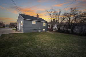 Back house at dusk with a patio area, a yard, and central AC unit