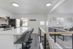 Kitchen featuring white subway backsplash, stainless steel appliances, dark LVP wood-type flooring, white cabinetry, and a island