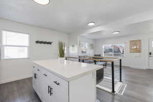 Kitchen with a kitchen island, dark LVP wood-style flooring, white cabinetry, and a textured ceiling