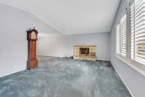 Unfurnished living room featuring dark carpet, lofted ceiling, and a stone fireplace