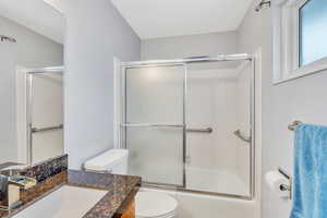 Full bathroom featuring vanity, bath / shower combo with glass door, and toilet