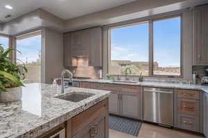 Kitchen featuring light tile patterned floors, backsplash, stainless steel dishwasher, and sink