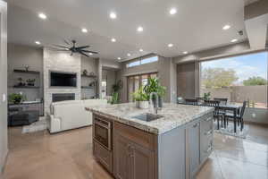 Kitchen featuring a kitchen island with sink, a stone fireplace, sink, ceiling fan, and gray cabinets