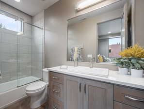 Full bathroom with a wealth of natural light, vanity, enclosed tub / shower combo, and toilet