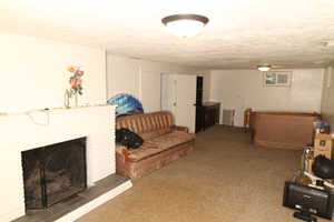 Carpeted living room featuring radiator heating unit, a textured ceiling, and a brick fireplace