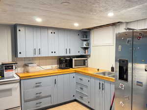 Kitchen featuring wooden counters, appliances with stainless steel finishes, gray cabinetry, and sink