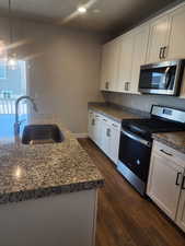 Kitchen with white cabinetry, sink, hanging light fixtures, dark wood-type flooring, and appliances with stainless steel finishes