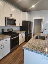 Kitchen with dark hardwood / wood-style flooring, sink, white cabinets, and appliances with stainless steel finishes