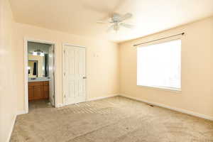 Unfurnished bedroom with ensuite bathroom, ceiling fan, and light carpet