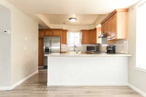 Kitchen featuring kitchen peninsula, appliances with stainless steel finishes, light wood-type flooring, and tasteful backsplash