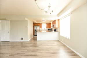 Kitchen with kitchen peninsula, stainless steel appliances, sink, an inviting chandelier, and light hardwood / wood-style floors