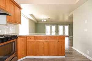 Kitchen featuring dark hardwood / wood-style flooring, a notable chandelier, kitchen peninsula, stainless steel electric stove, and exhaust hood