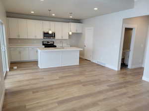 Kitchen with sink, black gas stove, hanging light fixtures, and an island with sink