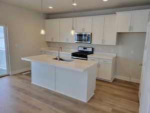 Kitchen with pendant lighting, white cabinets, a center island with sink, sink, and stainless steel appliances