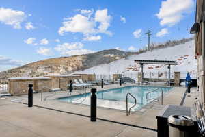 Snow covered pool featuring a mountain view and a patio area