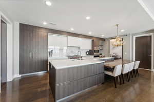 Kitchen with sink, hanging light fixtures, dark hardwood / wood-style floors, a kitchen island with sink, and white cabinets