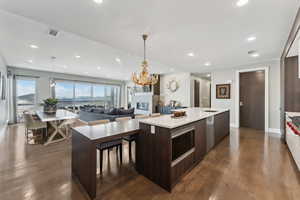 Kitchen with appliances with stainless steel finishes, dark hardwood / wood-style flooring, a kitchen island with sink, sink, and hanging light fixtures