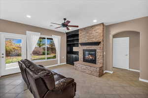 Tiled living room with a stone fireplace, a wealth of natural light, built in features, and ceiling fan