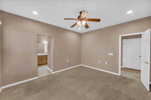 Unfurnished bedroom with connected bathroom, light colored carpet, and ceiling fan