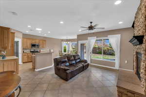 Living room with a stone fireplace, light tile patterned floors, and ceiling fan with notable chandelier