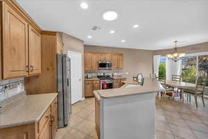 Kitchen with sink, stainless steel appliances, a notable chandelier, backsplash, and an island with sink