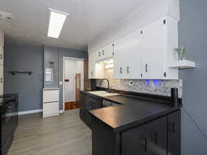 Kitchen featuring electric range, sink, tasteful backsplash, light hardwood / wood-style floors, and white cabinets