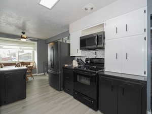 Kitchen with backsplash, white cabinets, ceiling fan, light wood-type flooring, and stainless steel appliances