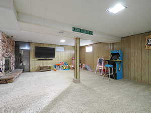 Recreation room with a stone fireplace, wooden walls, and carpet floors