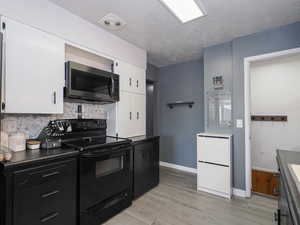 Kitchen featuring light wood-type flooring, backsplash, black electric range oven, a textured ceiling, and white cabinetry