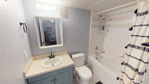 Full bathroom featuring vanity, shower / bath combination with curtain, toilet, and a textured ceiling