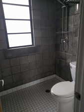 Bathroom featuring toilet, tile patterned flooring, and tiled shower