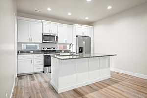 Kitchen with white cabinets, dark stone countertops, stainless steel appliances, and an island with sink