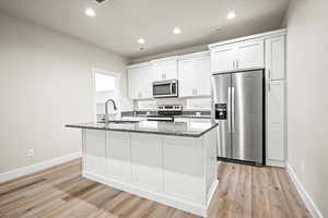 Kitchen with appliances with stainless steel finishes, light wood-type flooring, a kitchen island with sink, sink, and white cabinetry