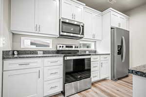 Kitchen with dark stone countertops, white cabinetry, stainless steel appliances, and light hardwood / wood-style flooring