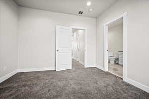 Unfurnished bedroom with dark colored carpet and ensuite bathroom