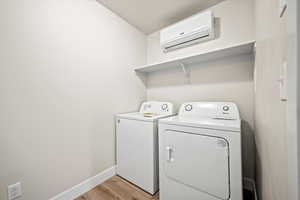 Washroom featuring separate washer and dryer, light hardwood / wood-style floors, and an AC wall unit