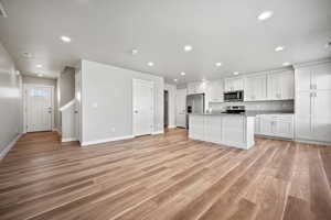 Kitchen featuring light hardwood / wood-style flooring, white cabinets, a center island with sink, and appliances with stainless steel finishes