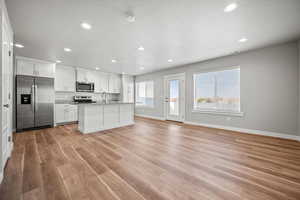 Kitchen with light stone counters, white cabinets, stainless steel appliances, and light wood-type flooring