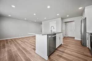 Kitchen featuring appliances with stainless steel finishes, light wood-type flooring, sink, white cabinets, and an island with sink