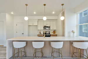 Kitchen featuring light wood-type flooring, stainless steel appliances, white cabinetry, and hanging light fixtures