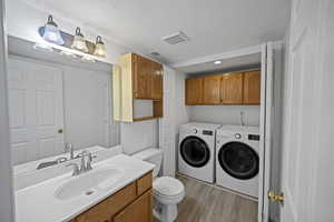 Clothes washing area featuring cabinets, sink, light wood-type flooring, a textured ceiling, and washing machine and clothes dryer