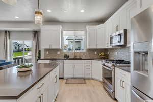 Kitchen featuring sink, hanging light fixtures, stainless steel appliances, white cabinets, and light wood-type flooring