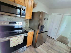 Kitchen featuring light stone countertops, stainless steel appliances, tasteful backsplash, and light hardwood / wood-style floors