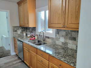 Kitchen featuring sink, stainless steel dishwasher, decorative backsplash, light stone countertops, and light hardwood / wood-style floors