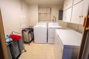 Laundry room featuring washing machine and clothes dryer, electric panel, and cabinets