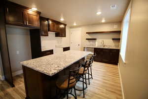 Kitchen with a center island, light stone counters, light wood-type flooring, and sink