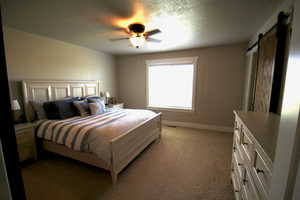 Bedroom with ceiling fan, a barn door, light colored carpet, and a textured ceiling