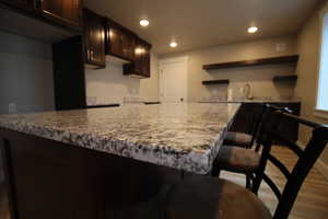 Kitchen featuring sink, light stone counters, a kitchen bar, dark brown cabinets, and hardwood / wood-style flooring