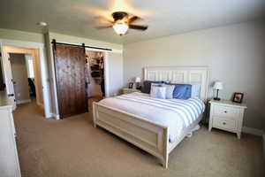 Bedroom featuring light colored carpet, ceiling fan, a barn door, a spacious closet, and a closet