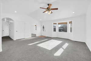 Unfurnished living room featuring carpet flooring, vaulted ceiling, and ceiling fan